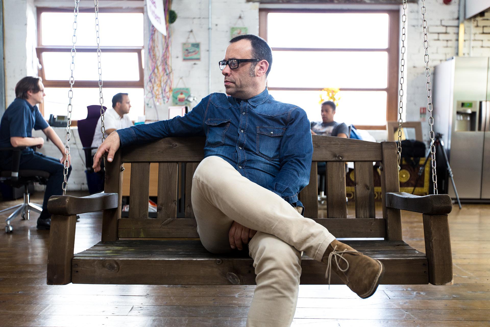Homem sentado em cadeira de balanço em momento de descompressão em espaço coworking